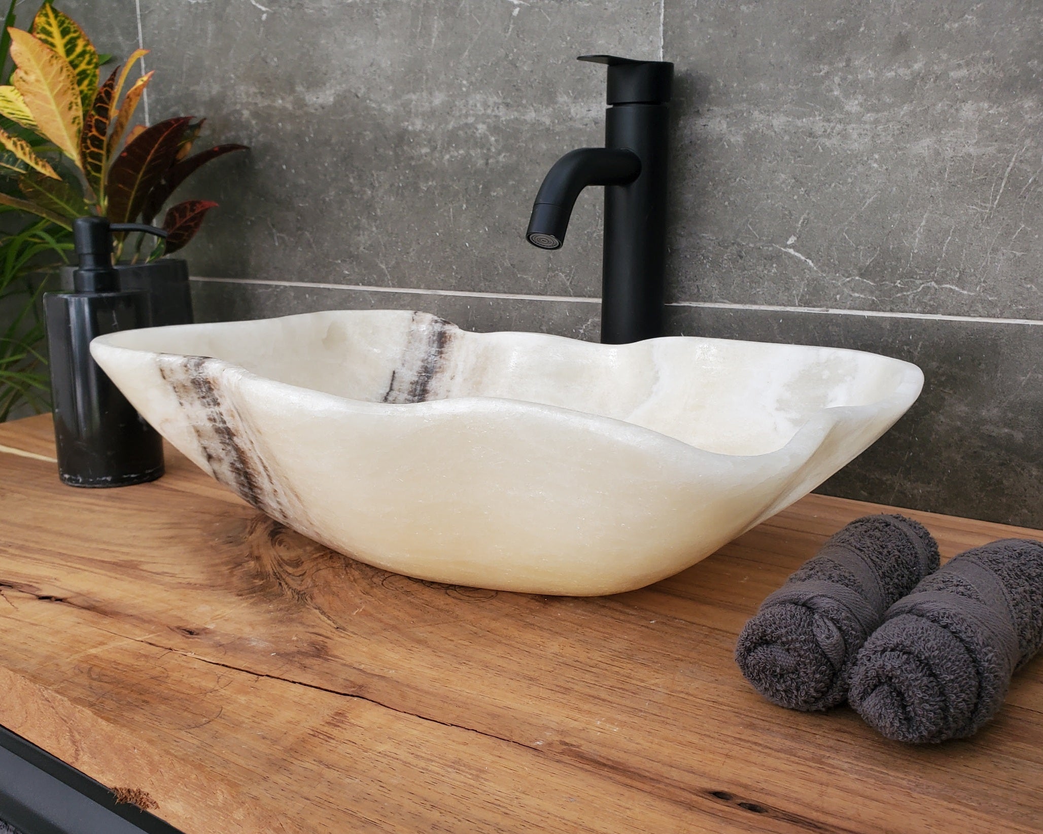 Bathroom vanity with a white stone sink, black faucet, and towels on a wooden countertop.